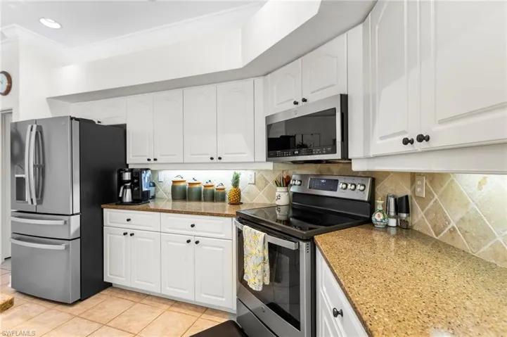 Kitchen with appliances with stainless steel finishes, light tile patterned floors, white cabinets, backsplash, and crown molding
