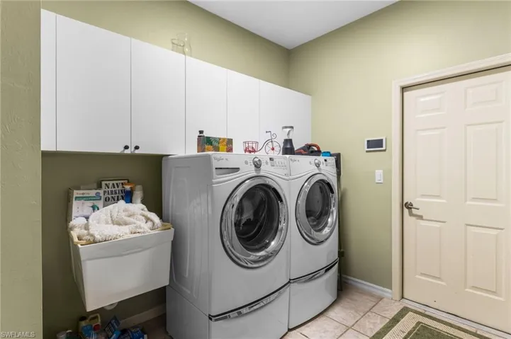 Washroom featuring light tile patterned floors, baseboards, cabinet space, and separate washer and dryer