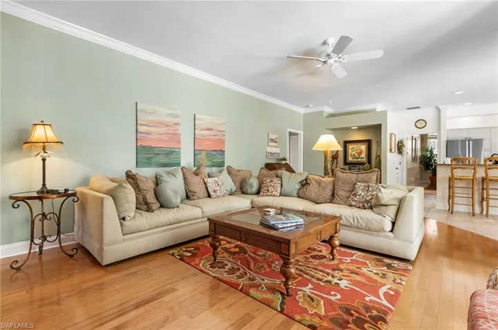 Living area featuring hardwood / wood-style flooring, a ceiling fan, ornamental molding, and baseboards