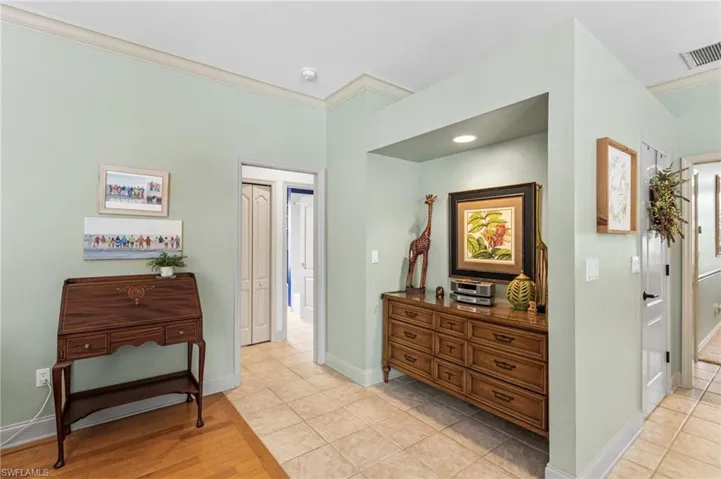 Corridor with light wood-style floors, baseboards, visible vents, and ornamental molding