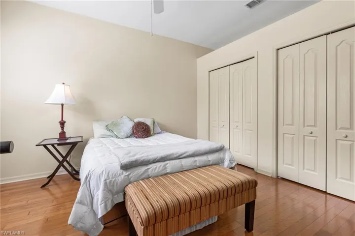Bedroom with visible vents, two closets, wood finished floors, baseboards, and ceiling fan