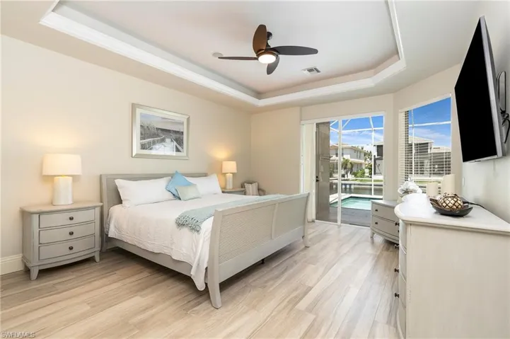 Bedroom with a tray ceiling, light wood-type flooring, access to exterior, visible vents, and ceiling fan