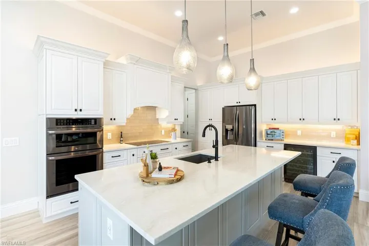 Kitchen with wine cooler, a sink, a breakfast bar, appliances with stainless steel finishes, and visible vents