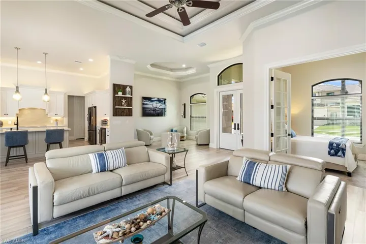 Living area with a tray ceiling, light wood-style flooring, ceiling fan, and crown molding