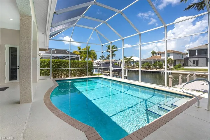 Outdoor pool featuring glass enclosure, a water view, a patio, and a residential view