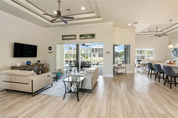 Living room featuring a tray ceiling, crown molding, light wood-type flooring, visible vents, and ceiling fan