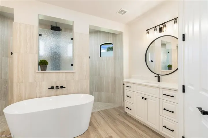 Full bath with vanity, tile walls, visible vents, a freestanding bath, and a walk in shower