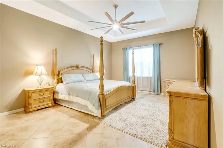 Bedroom with a raised ceiling, ceiling fan, baseboards, and light tile patterned floors