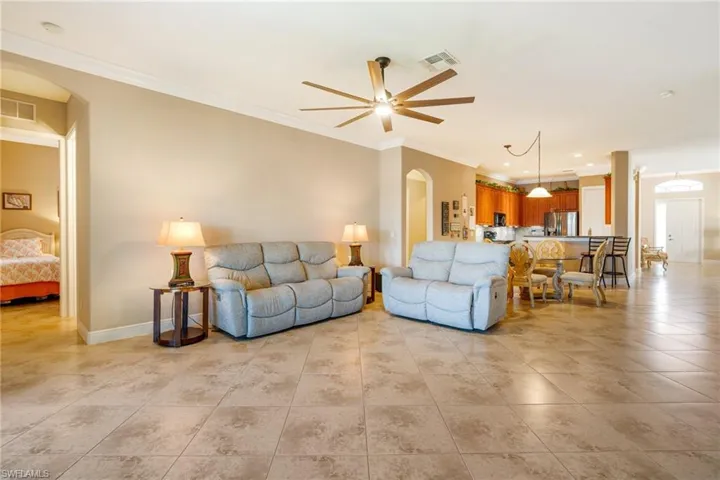 Living area with arched walkways, a ceiling fan, visible vents, and crown molding