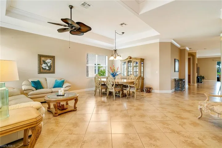 Living room with a raised ceiling, visible vents, crown molding, and light tile patterned flooring