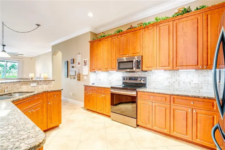 Kitchen with arched walkways, light tile patterned floors, a sink, appliances with stainless steel finishes, and crown molding