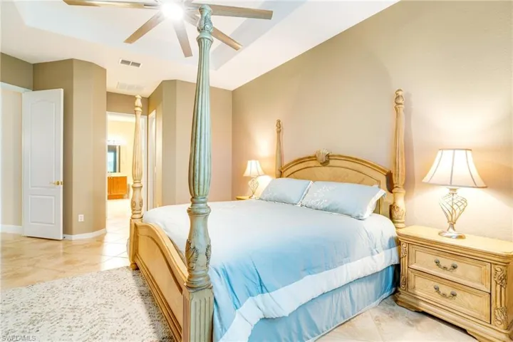 Bedroom with ensuite bath, visible vents, a raised ceiling, and baseboards
