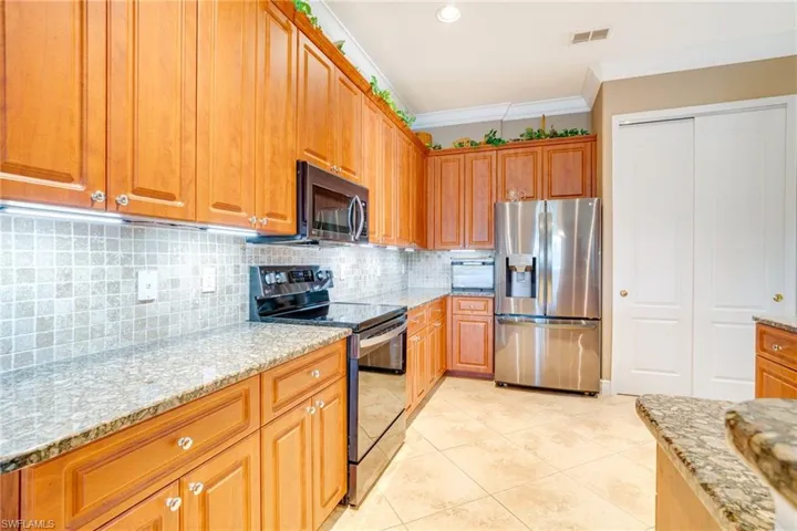 Kitchen with light stone counters, electric stove, crown molding, stainless steel refrigerator with ice dispenser, and visible vents
