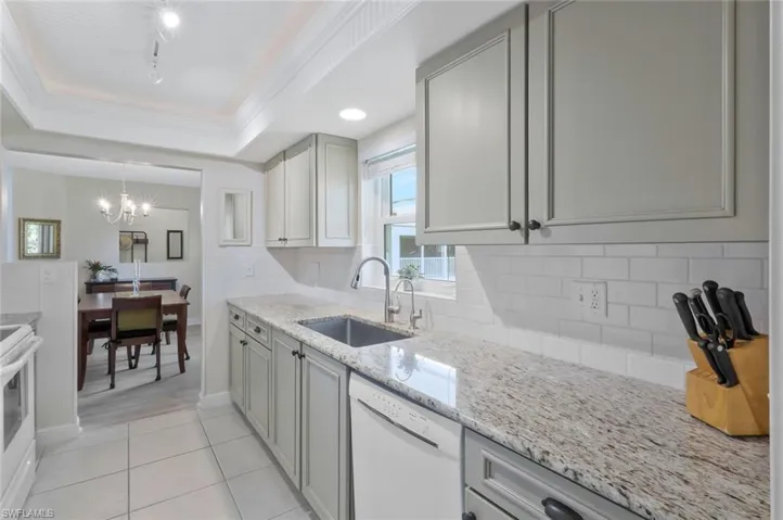 Kitchen facing the dining room.  The kitchen features a tray ceiling, wood cabinetry, granite countertops, subway tile backsplash, tile flooring and white appliances.