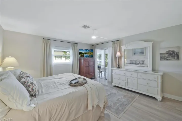 Primary bedroom with luxury vinyl flooring, ceiling fan, access to the primary bathroom and sliding door access to the lanai.