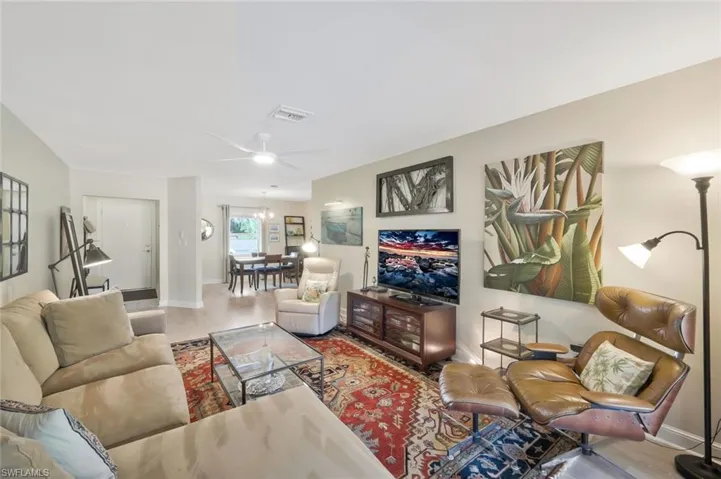 Family room facing dining area and front door entry, with ceiling fan and luxury vinyl floors with sliding doors to the lanai (not shown).