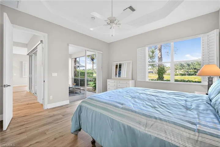 Bedroom featuring light wood finished floors, access to outside, a raised ceiling, and a ceiling fan