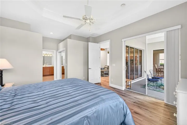 Bedroom featuring a raised ceiling, light wood-style flooring, access to outside, connected bathroom, and crown molding