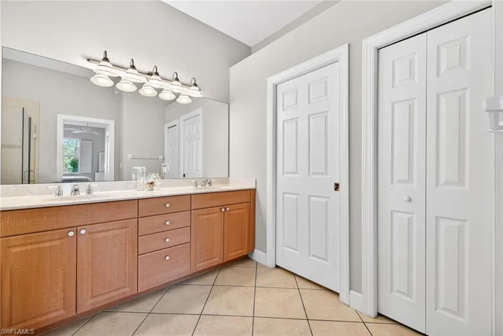 Full bathroom featuring double vanity, light tile patterned floors, a closet, ceiling fan, and a stall shower