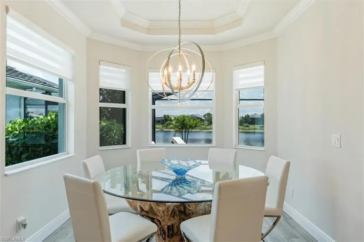 Dining room with a chandelier, a tray ceiling, crown molding, a water view, and light hardwood / wood-style flooring