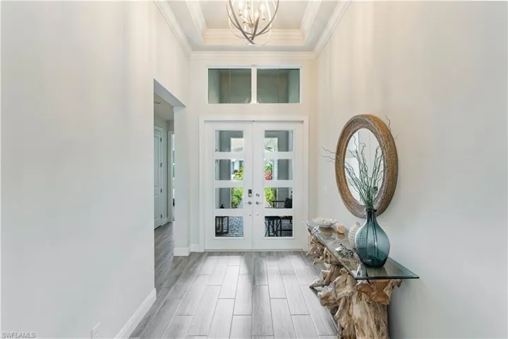 Foyer with crown molding, an inviting chandelier, and french doors