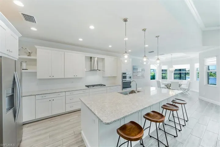 Kitchen featuring wall chimney range hood, hanging light fixtures, white cabinets, and appliances with stainless steel finishes