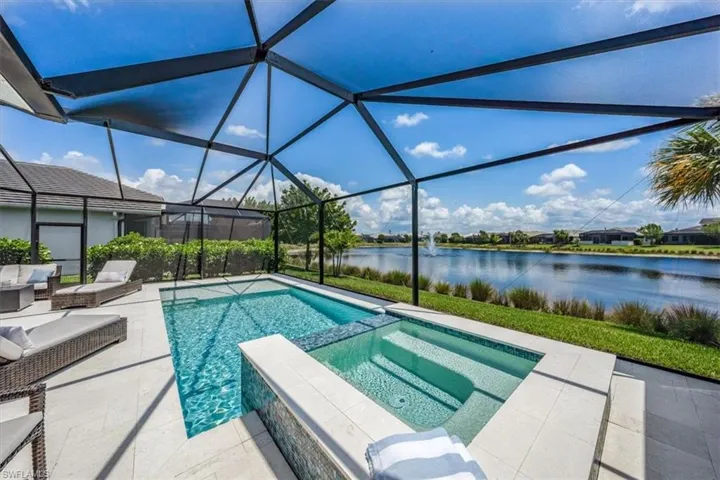 View of pool featuring a patio area, an in ground hot tub, glass enclosure, and a water view