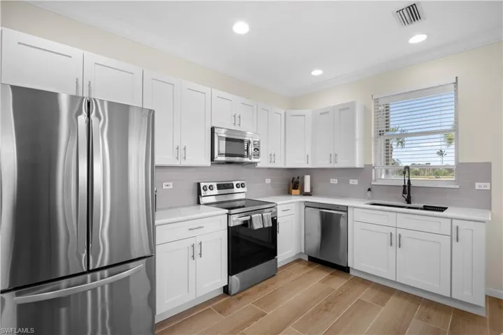 Kitchen featuring stainless steel appliances, ornamental molding, white cabinets, wood tiled floors, and recessed lighting