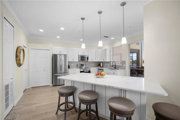 Kitchen featuring a breakfast bar, a peninsula, stainless steel appliances, wood tiled floors, and decorative light fixtures