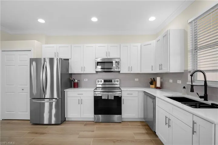 Kitchen with stainless steel appliances, white cabinets, crown molding, wood finish floors, and backsplash