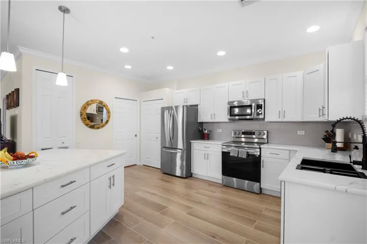 Kitchen featuring stainless steel appliances, crown molding, wood finish floors, white cabinetry, and decorative backsplash