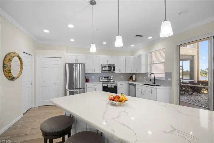 Kitchen featuring stainless steel appliances, ornamental molding, pendant lighting, white cabinetry, and a kitchen breakfast bar