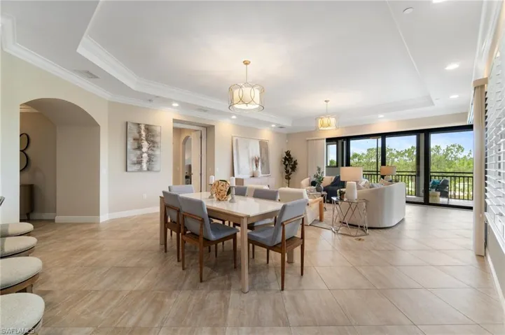 Dining room featuring a raised ceiling, arched walkways, light tile patterned floors, ornamental molding, and baseboards
