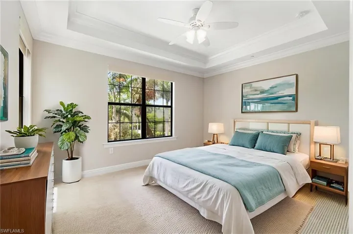 Bedroom featuring a tray ceiling, crown molding, baseboards, carpet, and a ceiling fan