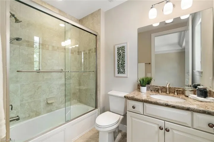 Bathroom with vanity, toilet, ornamental molding, bath / shower combo with glass door, and tile patterned floors