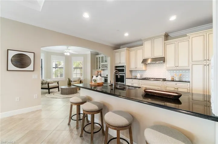 Kitchen featuring cream cabinetry, arched walkways, under cabinet range hood, cooktop, and a sink