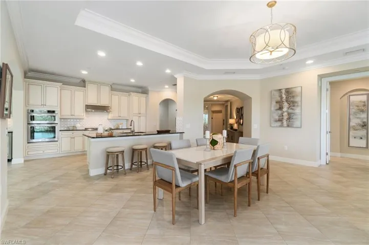 Dining space featuring arched walkways, ornamental molding, recessed lighting, light tile patterned floors, and a tray ceiling