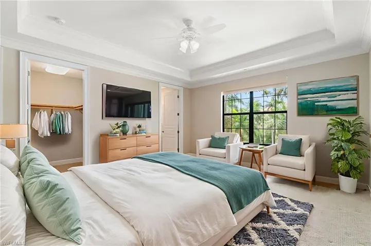 Bedroom featuring a raised ceiling, crown molding, light colored carpet, baseboards, and a closet