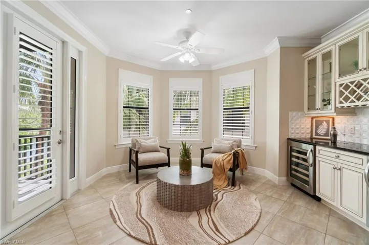 Sitting room featuring wine cooler, a dry bar, ornamental molding, baseboards, and light tile patterned floors