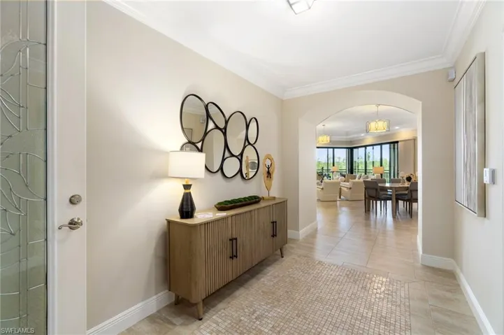 Hall featuring arched walkways, crown molding, baseboards, and light tile patterned floors