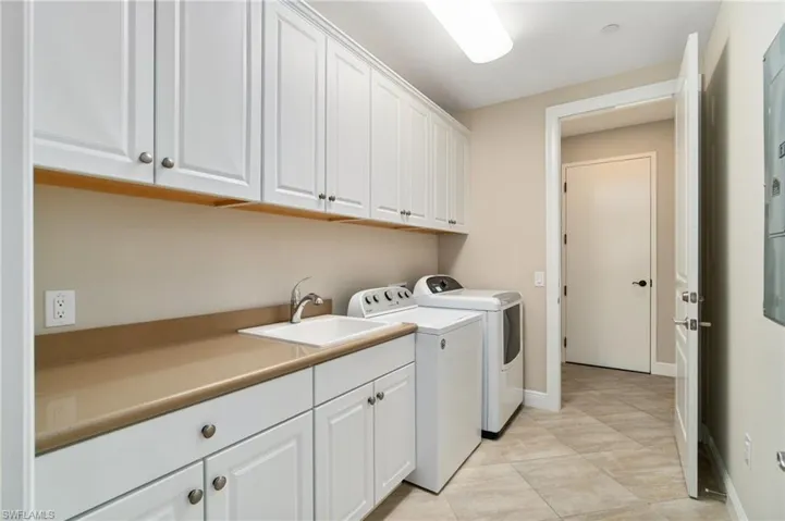 Laundry area featuring separate washer and dryer, cabinet space, and baseboards