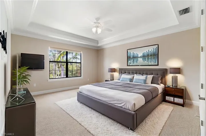 Bedroom featuring a tray ceiling, light carpet, baseboards, and crown molding