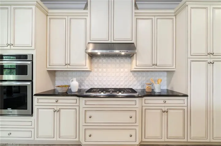 Kitchen with cream cabinetry, under cabinet range hood, appliances with stainless steel finishes, and backsplash