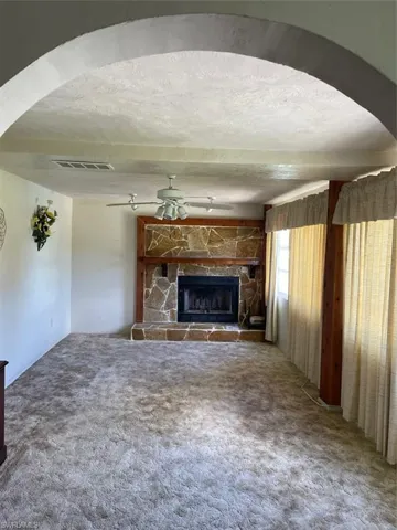 Unfurnished living room featuring a stone fireplace, carpet, a textured ceiling, and ceiling fan