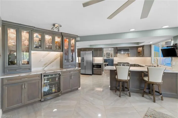 Kitchen featuring beverage cooler, stainless steel appliances, a breakfast bar, wall chimney range hood, and tasteful backsplash