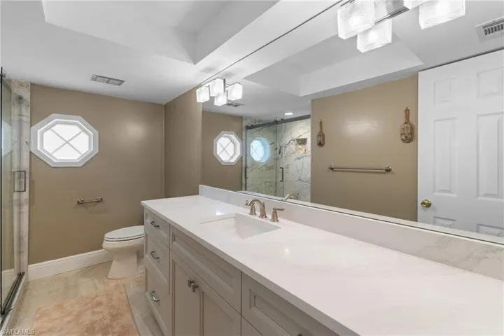 Bathroom featuring toilet, visible vents, vanity, baseboards, and a shower stall
