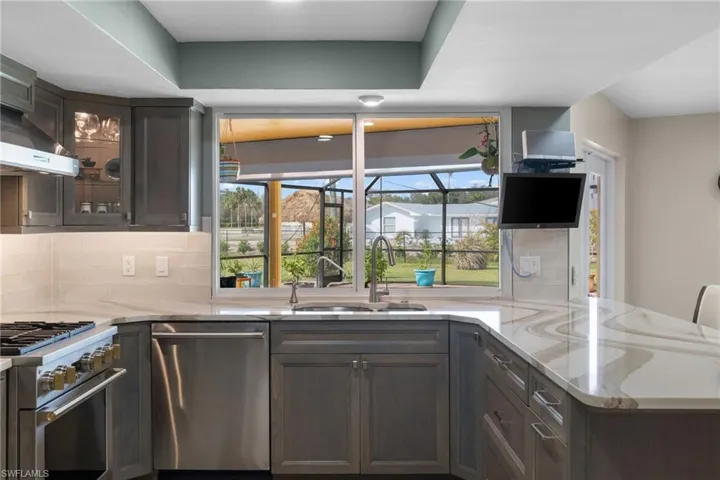 Kitchen featuring a peninsula, appliances with stainless steel finishes, light stone counters, and a sink