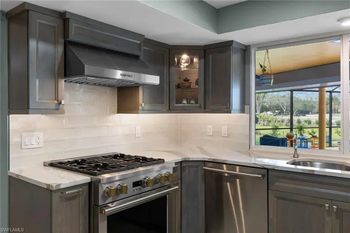 Kitchen with wall chimney range hood, light stone counters, stainless steel appliances, and backsplash