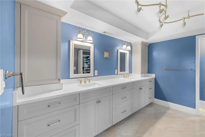 Bathroom featuring a raised ceiling, a sink, baseboards, and double vanity