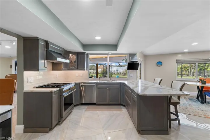 Kitchen featuring a breakfast bar, stainless steel appliances, tasteful backsplash, wall chimney range hood, and a peninsula